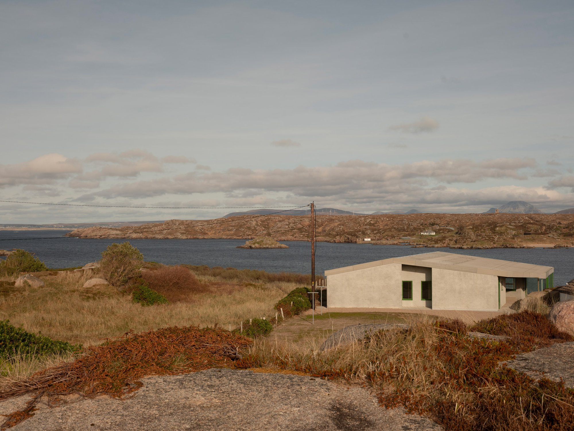 만(bay)을 등지고 선 Cruit Island House 외관, 그린 창호와 화이트 렌더 마감