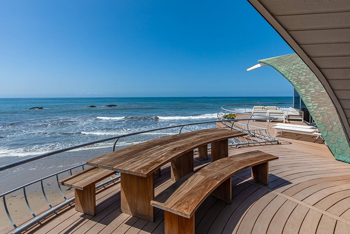곡선 원목 벤치와 물고기 비늘 모양 지붕이 보이는 Wave House 데크