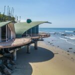 말리부 해변 기둥 위에 올라선 Wave House의 물결 모양 구리 지붕과 곡선 데크