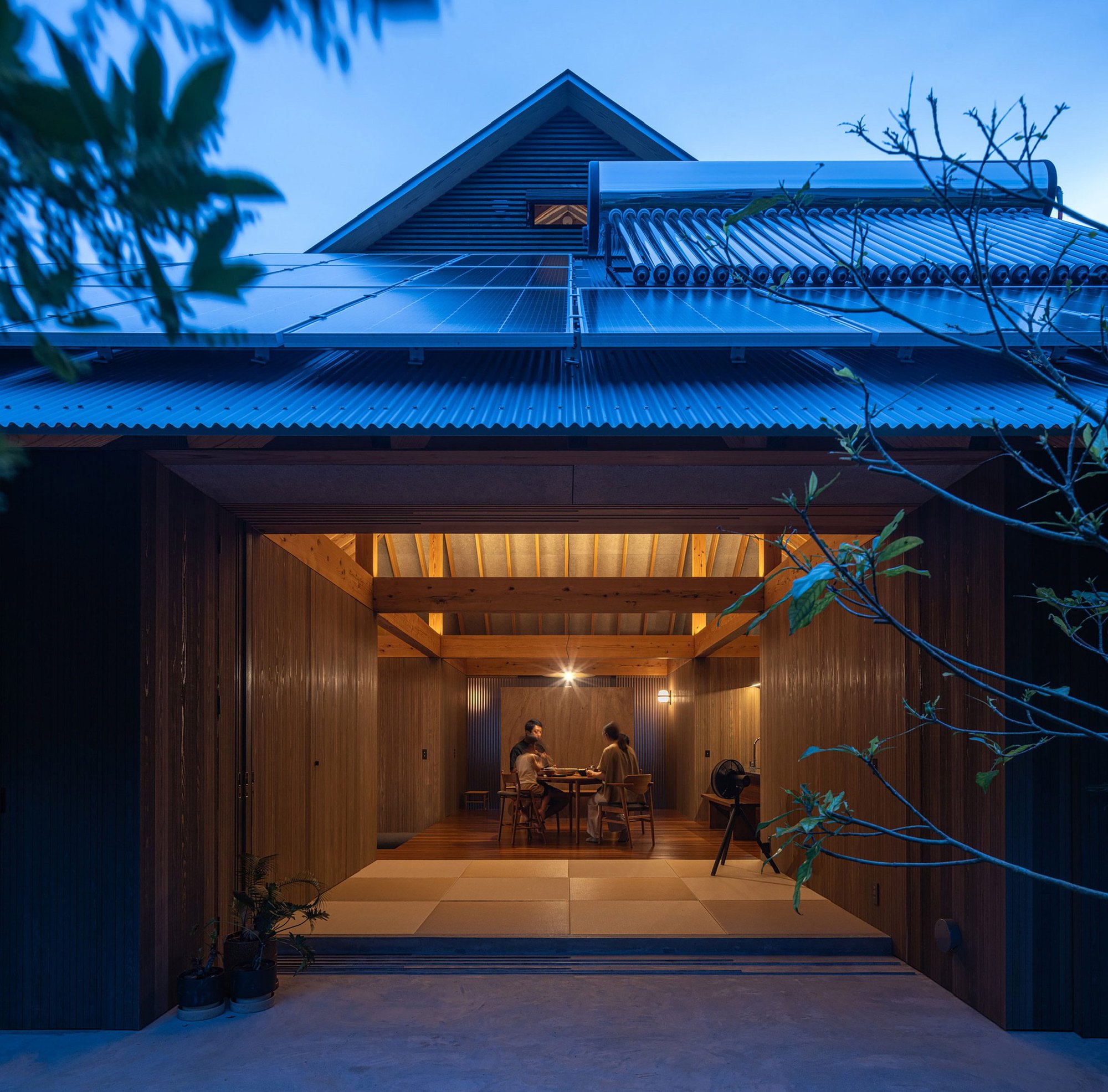지붕 위 태양광 패널과 태양열 온수기, 해질녘 다이닝 공간이 보이는 Amami House