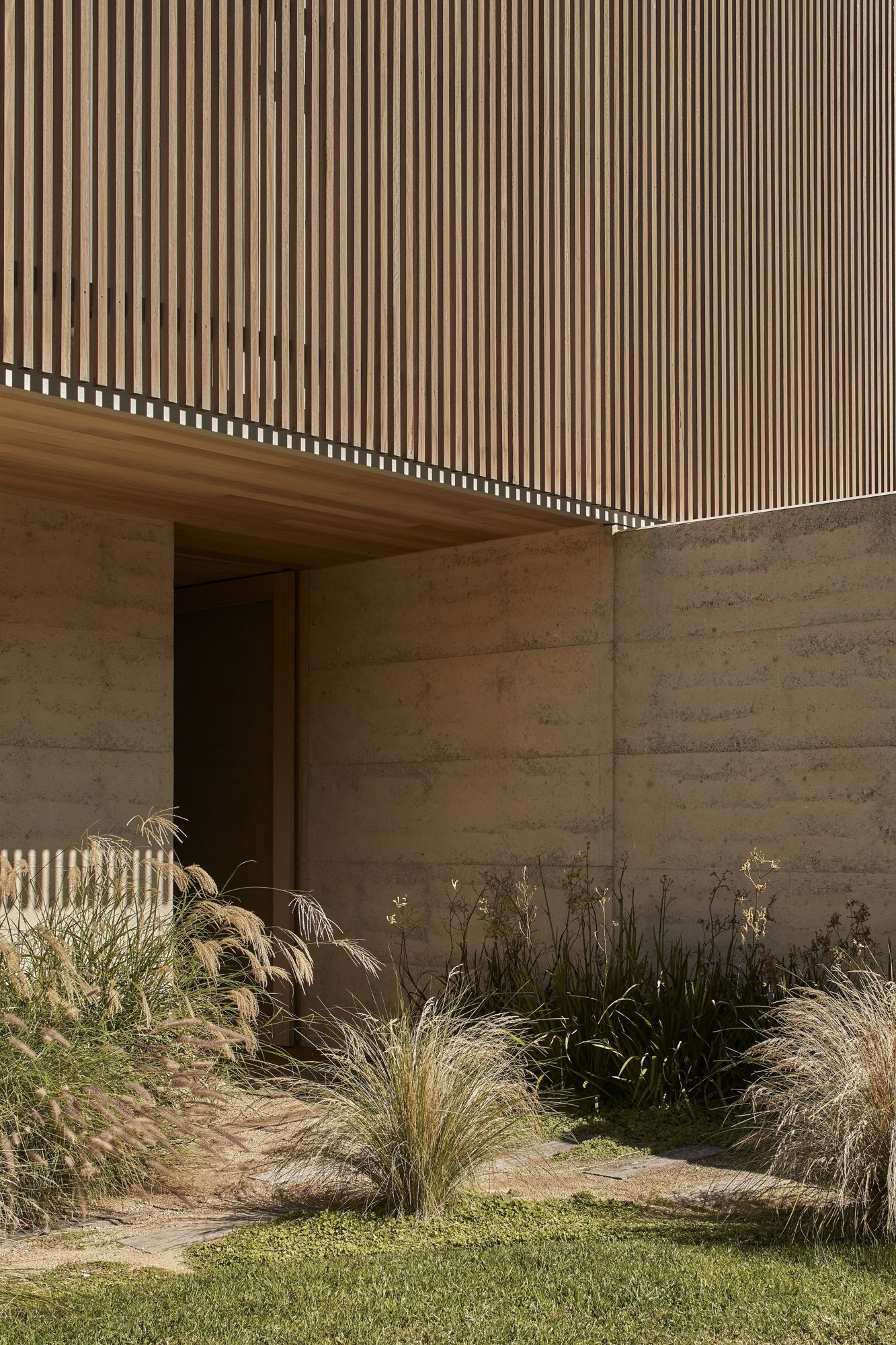 목재 스크린 아래 흙다짐 벽으로 둘러싼 Barwon Dunes House 현관 진입부