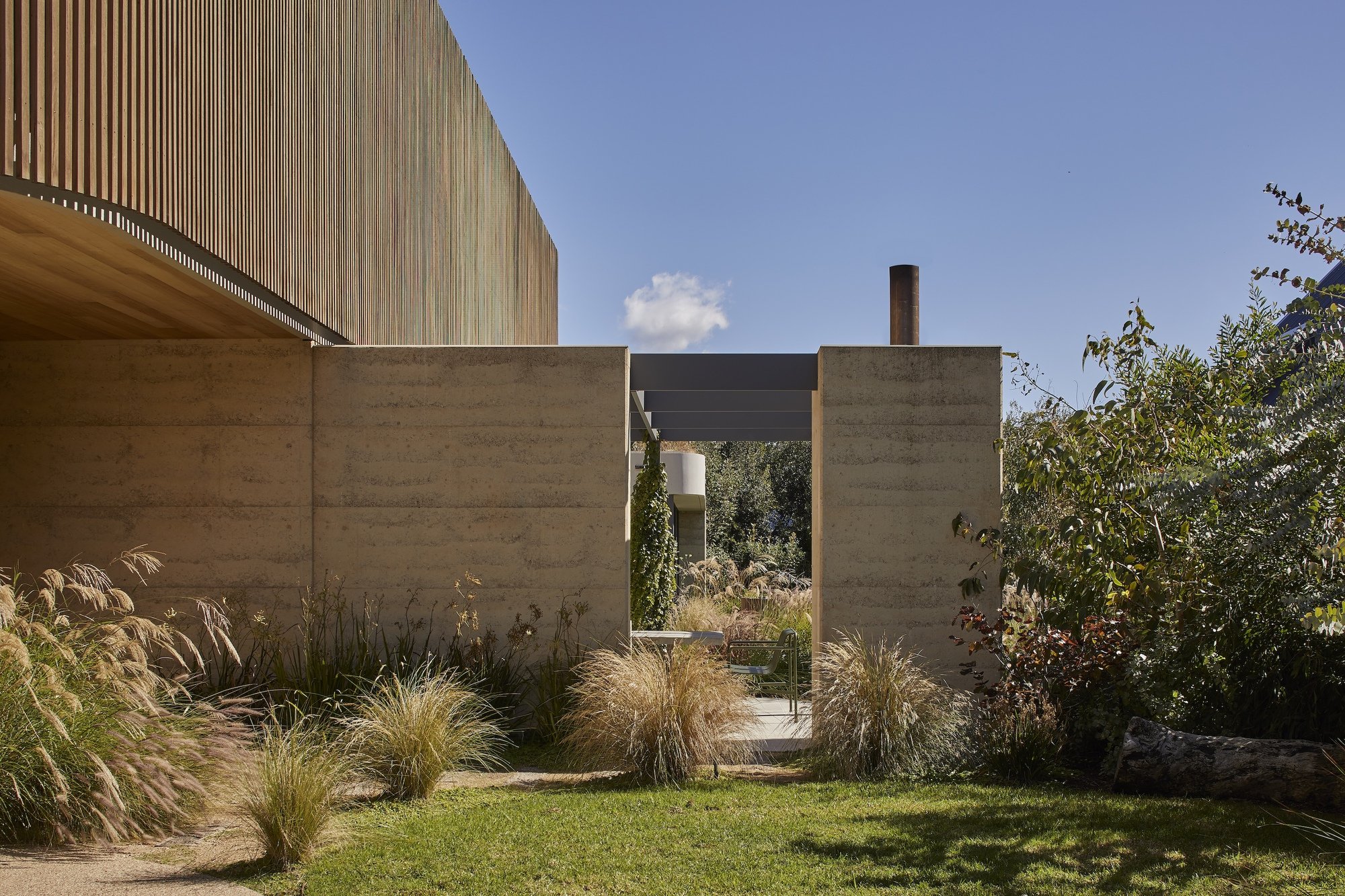 흙다짐 벽과 굴뚝이 정원 너머로 보이는 Barwon Dunes House 외관